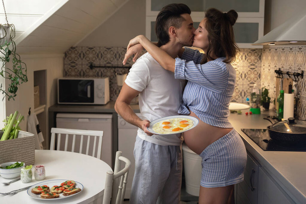 Young and happy couple waiting for a baby. Husband and his pregnant wife on the kitchen during breakfast time. - Fotoğraf, Görsel