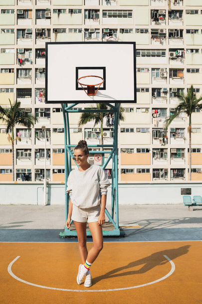 Fiatal, stílusos nő pózol a Choi Hung Birtok kosárlabdapályáján Hong Kong városban. - Fotó, kép