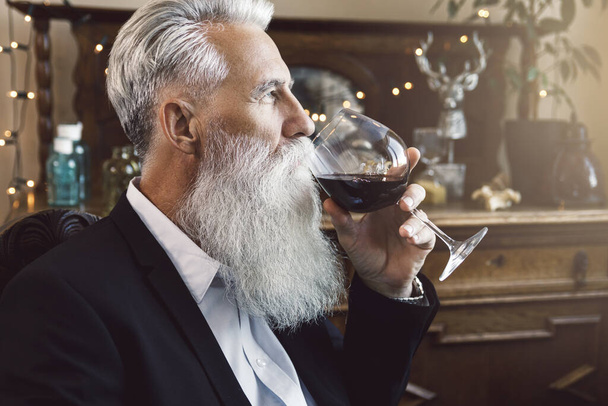 Stylish and handsome bearded senior man drinking red wine - 写真・画像