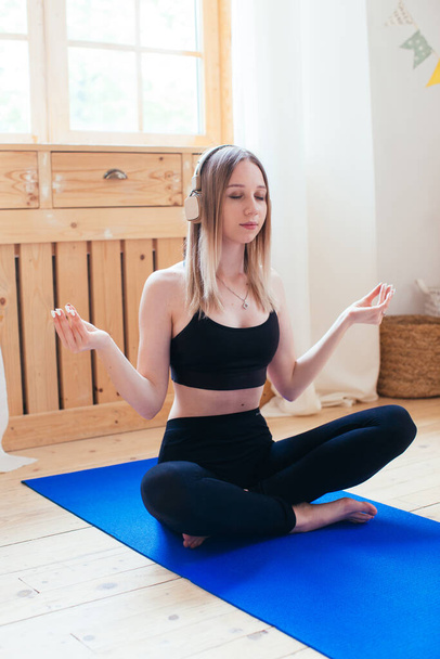 Jonge vrouw die yoga beoefent en thuis naar muziek luistert. meditatie met telefoon app - Foto, afbeelding