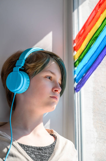Smutná puberťačka ve sluchátkách poslouchající hudbu, opírající se o okno. Chybí jí přátelé.. - Fotografie, Obrázek