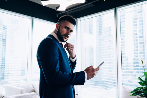 Busy handsome male manager in business style clothing communicating on mobile phone with colleagues while brainstorming and looking at camera at office  - Фото, изображение