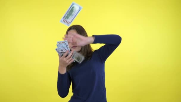 Rich teenager girl in a blue sweater scatters lot of money on yellow background - Filmmaterial, Video
