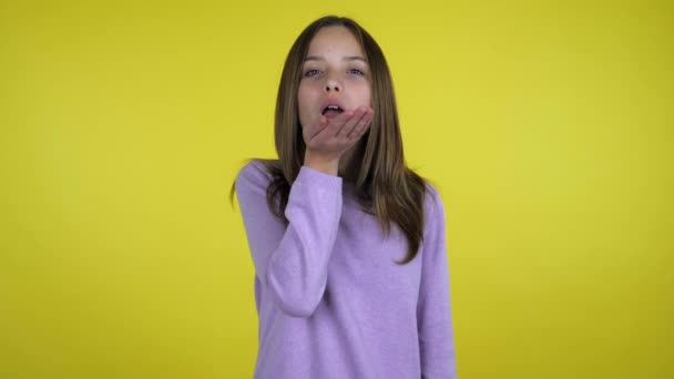 Beautiful teenager girl in a pink sweater sends an air kiss on yellow background - Séquence, vidéo