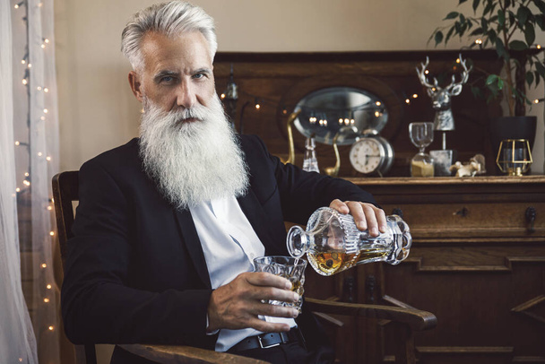 Stylish and handsome bearded senior man pouring whiskey into the glass - Fotó, kép