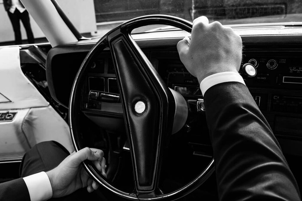 Retro car. Black. On Polished bumpers. The man keeps his hands on the steering wheel. Black and white photo. - 写真・画像