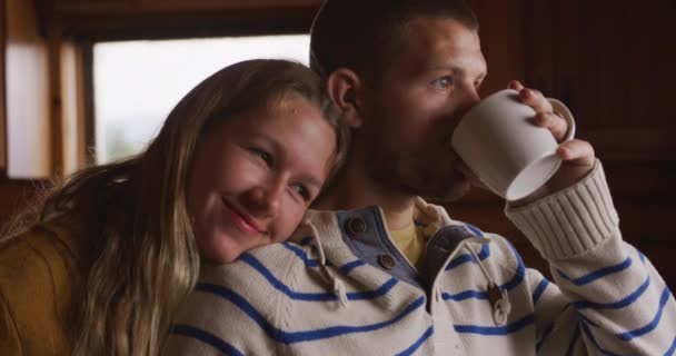 Caucasian couple spending time at home together, social distancing and self isolation in quarantine lockdown, standing in a kitchen, embracing, the man drinking from a mug in slow motion - Záběry, video