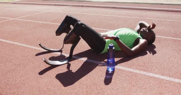 Fit, disabled mixed race man with prosthetic legs lying on race track, resting in slow motion - Metraje, vídeo