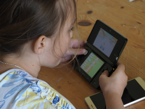 Ένα κορίτσι παίζει ένα παιχνίδι σε μια κονσόλα χειρός - Φωτογραφία, εικόνα