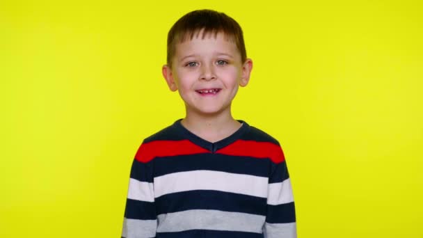 Μικρό αγόρι κοιτάζει την κάμερα και γελάει σε ένα κίτρινο φόντο με αντίγραφο χώρο - Πλάνα, βίντεο