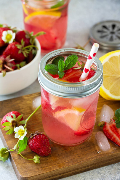 夏の飲み物は爽やか。軽い石のカウンターの上に新鮮なイチゴ、氷、レモンが飾られています。. - 写真・画像
