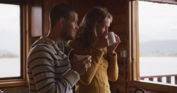 Caucasian couple spending time at home together, social distancing and self isolation in quarantine lockdown, standing in a kitchen, holding mugs and drinking in slow motion - Video