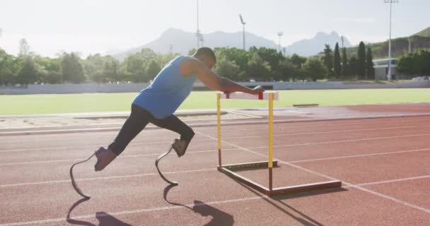 Fit, disabled mixed race man with prosthetic legs stretching with a hurdle in slow motion - Filmati, video