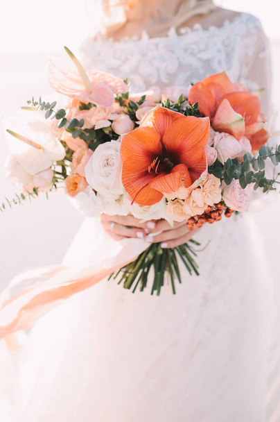 白い桃の色合いでアマリリス、アンスリウム、バラ、カーネーション、ユーカリの花嫁の花束のクローズアップ。レースの白いドレスの花嫁は彼女の手に花束を持っています。白い砂 - 写真・画像