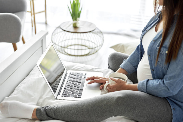 Έγκυος γυναίκα που χρησιμοποιεί φορητό υπολογιστή, ενώ κάθεται στο κρεβάτι - Φωτογραφία, εικόνα