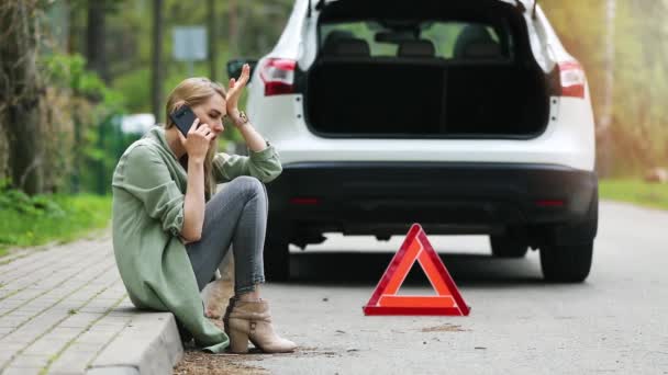 Frau sitzt am Straßenrand und ruft um Hilfe, weil kaputtes Auto - Filmmaterial, Video