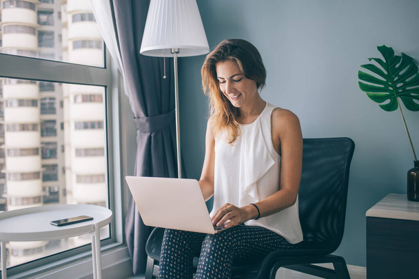 Skilled successful female freelancer doing distance job in home interior typing content text via laptop keyboard, happy woman playing online games via modern netbook during leisure in own apartment - Fotoğraf, Görsel