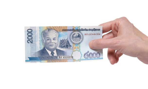 Mano femminile con una banconota da 2000 Kip isolata su sfondo bianco. Ritratto del Presidente Kaysone Phomevihane sui soldi
. - Foto, immagini