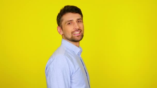 Hezký vousatý muž otočí hlavu ke kameře a usměje se na žlutém pozadí - Záběry, video
