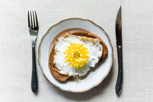 Imagem conceitual de tomar café da manhã com torrada de ovo frito. Flor de crisântemo amarelo em vez de gema servida em uma placa branca
 - Foto, Imagem