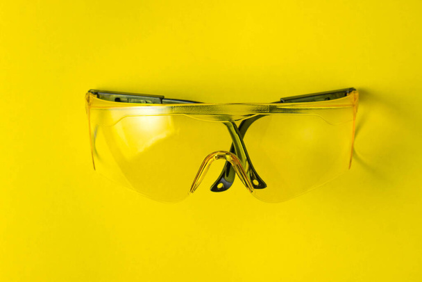 Gafas de seguridad amarillas sobre fondo amarillo. Las gafas están en medio de la foto. Foto arriba
 - Foto, Imagen