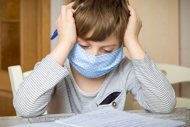 A first-grader boy in a mask is doing homework in quarantine because of a coronavirus. - Photo, Image
