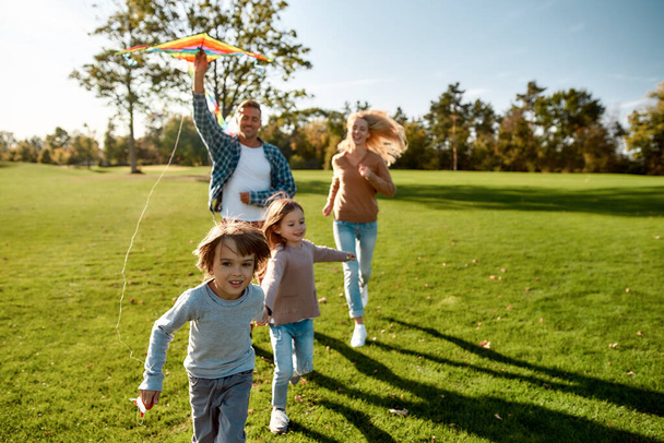 There are no words to describe how special kids are. Happy family playing a kite. Outdoor family weekend - Foto, afbeelding