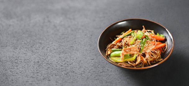 A bowl of wok noodles stands on a black table background - Foto, Imagem