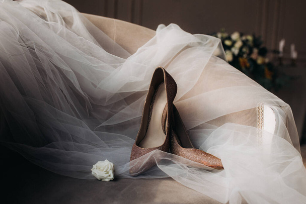 Wedding shoes for newlyweds with a veil close-up lying on a chair, next to a flower, beautiful layout. - Fotografia, imagem