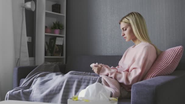 Young woman crying while watching movie on the grey sofa at home and wiping her tears with a napkin - Filmmaterial, Video