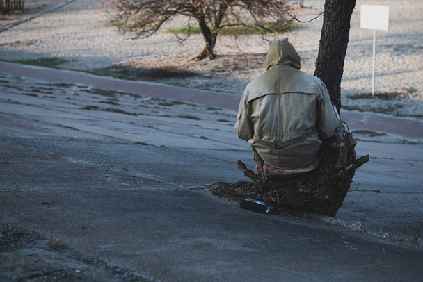 Osamělá neznámá osoba sedící na pařezu a čtoucí knihu. Muž ve starých špinavých šatech. Koncepce pandemické koronavirové izolace fotografie. Pohled zezadu. - Fotografie, Obrázek