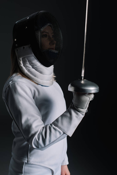 Side view of fencer in fencing mask holing rapier isolated on black  - Photo, image