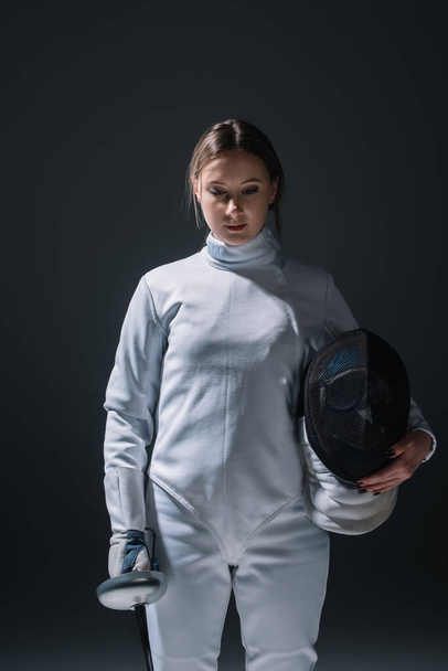 Beautiful woman holding rapier and fencing mask isolated on black  - Photo, Image