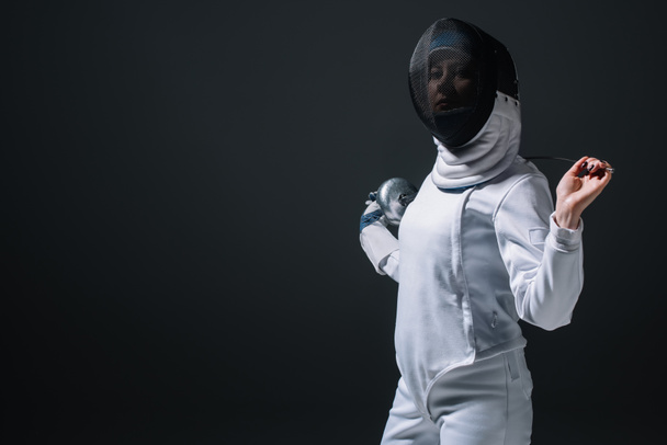 Fencer in fencing mask looking at camera while holding rapier isolated on black  - Foto, Imagem