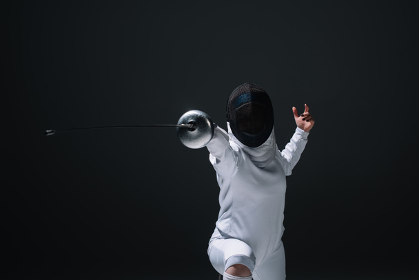 Fencer in fencing mask exercising with rapier isolated on black  - Photo, Image