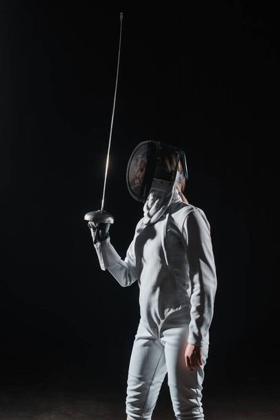 Šermíř v šermířské masce drží rapír izolovaný na černé  - Fotografie, Obrázek