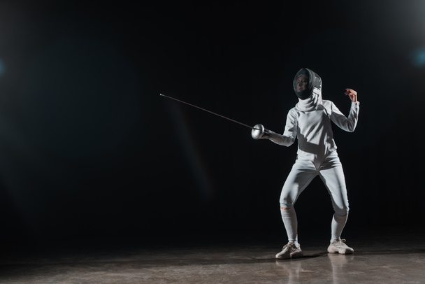 Fencer training met rapier onder spotlight op zwarte achtergrond - Foto, afbeelding