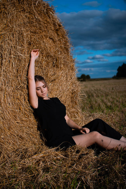 Style fashion on street. A girl with bundle hair in a earrings, black dress and white sneakers. Female portrait. Model posing. A girl in a dress on a haystack background. Fashion photography - Photo, image