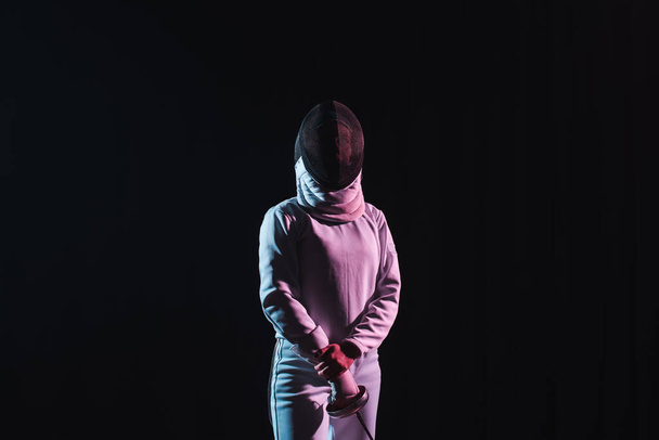 Esgrima em roupa de esgrima e máscara segurando rapier isolado em preto
  - Foto, Imagem