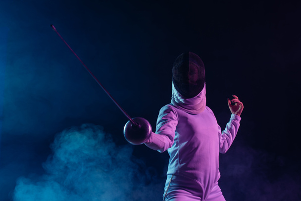 Low angle view of swordswoman fencing on black background with smoke and lighting  - Photo, Image