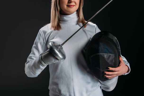 Cropped view of swordswoman holding rapier and fencing mask isolated on black  - Photo, Image
