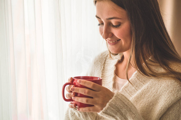 Женщина с чашкой горячего напитка у окна. Доброе утро с чаем. Зимнее время осенью
.  - Фото, изображение