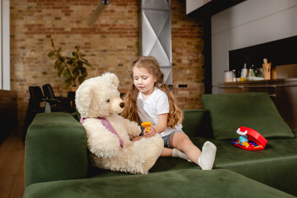 мила дитина тримає іграшку біля плюшевого ведмедя, граючи в лікарську гру
  - Фото, зображення