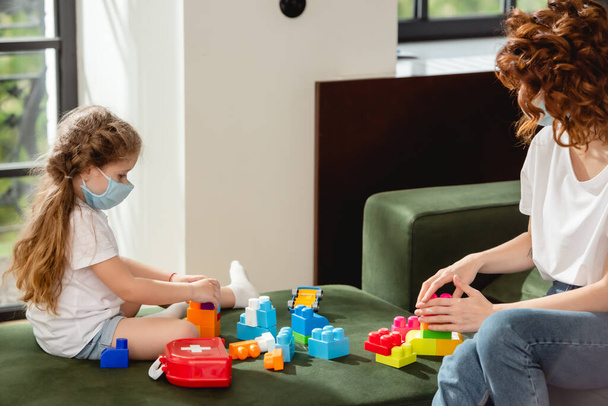 vörös hajú anya és gyerek orvosi maszk játszik építőkockák  - Fotó, kép