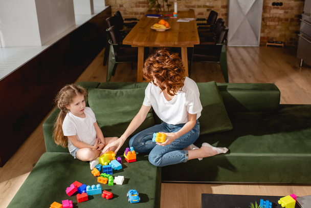 redhead mother and cute daughter playing building blocks in living room  - Fotó, kép