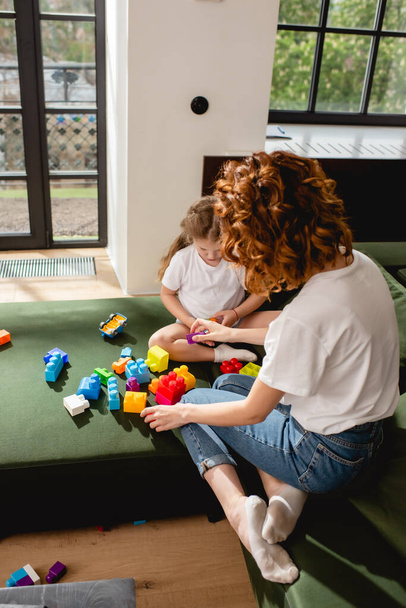 hátsó kilátás vörös hajú anya és aranyos lánya játszik építőkockák a nappaliban  - Fotó, kép