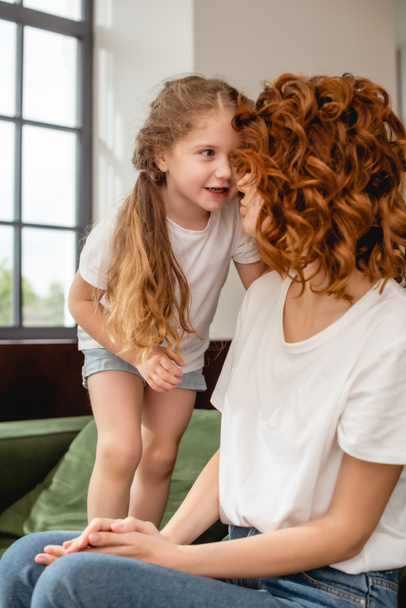 cute kid looking at curly mother sitting on sofa - Fotografie, Obrázek