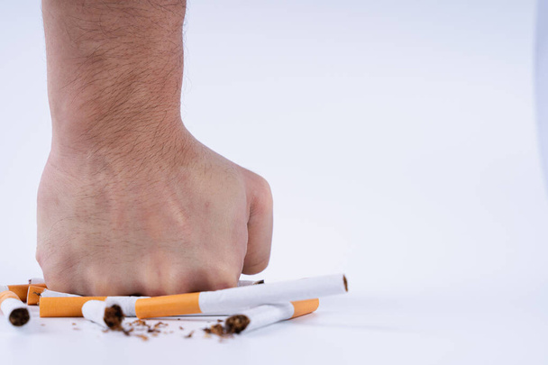 Arrête de fumer. Gros plan d'un homme brisant sa cigarette avec son poing. Journée du tabac. Cigarette sur fond blanc
. - Photo, image