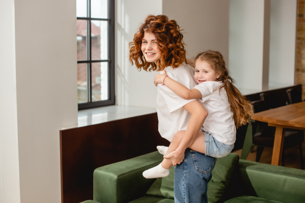 smiling and curly mother piggybacking cute daughter  - Foto, Imagem