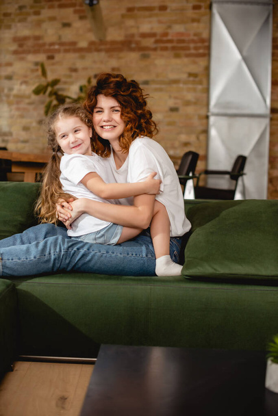 cute daughter hugging cheerful and curly mother  - Fotografie, Obrázek